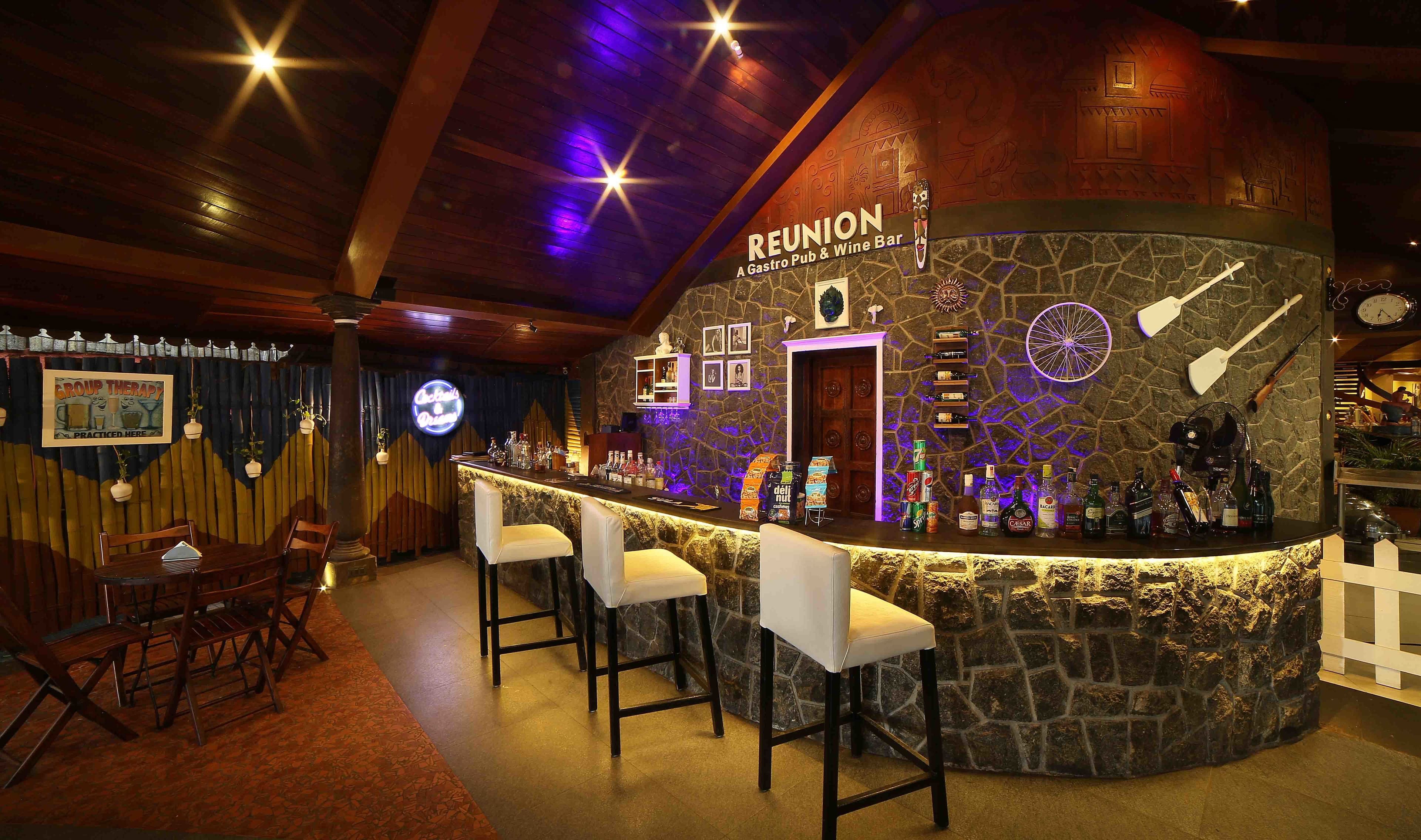 Zona de bar con pared de piedra, taburetes y una variedad de botellas.