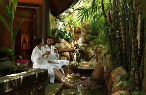 Dos personas sentadas junto a una fuente con plantas y rocas.