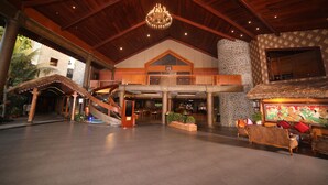Un hall espacioso con techo alto, una escalera central, una chimenea de piedra y una zona de estar con un mural.
