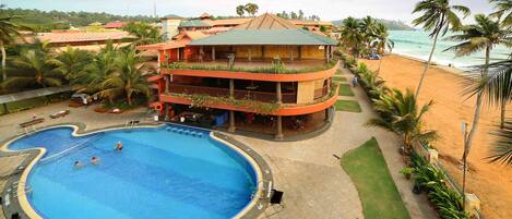 A hotel with a swimming pool, a beach view, and a multi-story building with balconies.