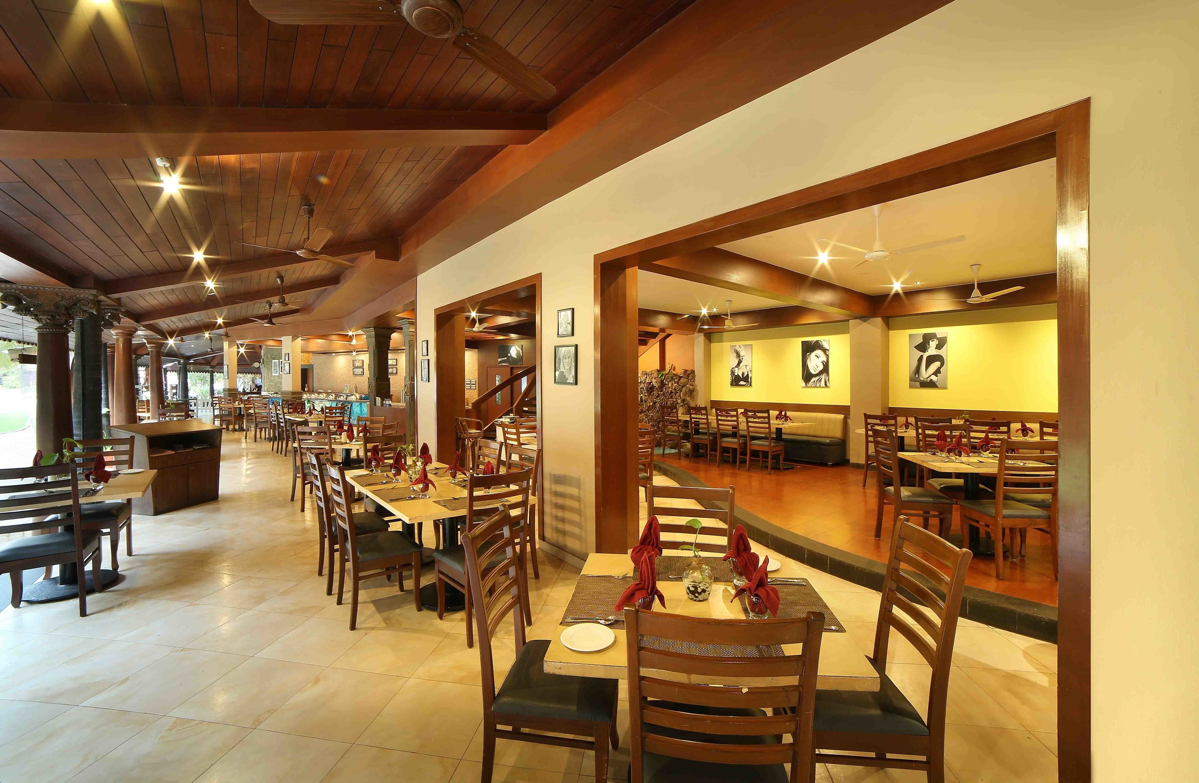 A spacious restaurant with wooden tables and chairs, a high ceiling with exposed beams, and framed artwork on the walls.