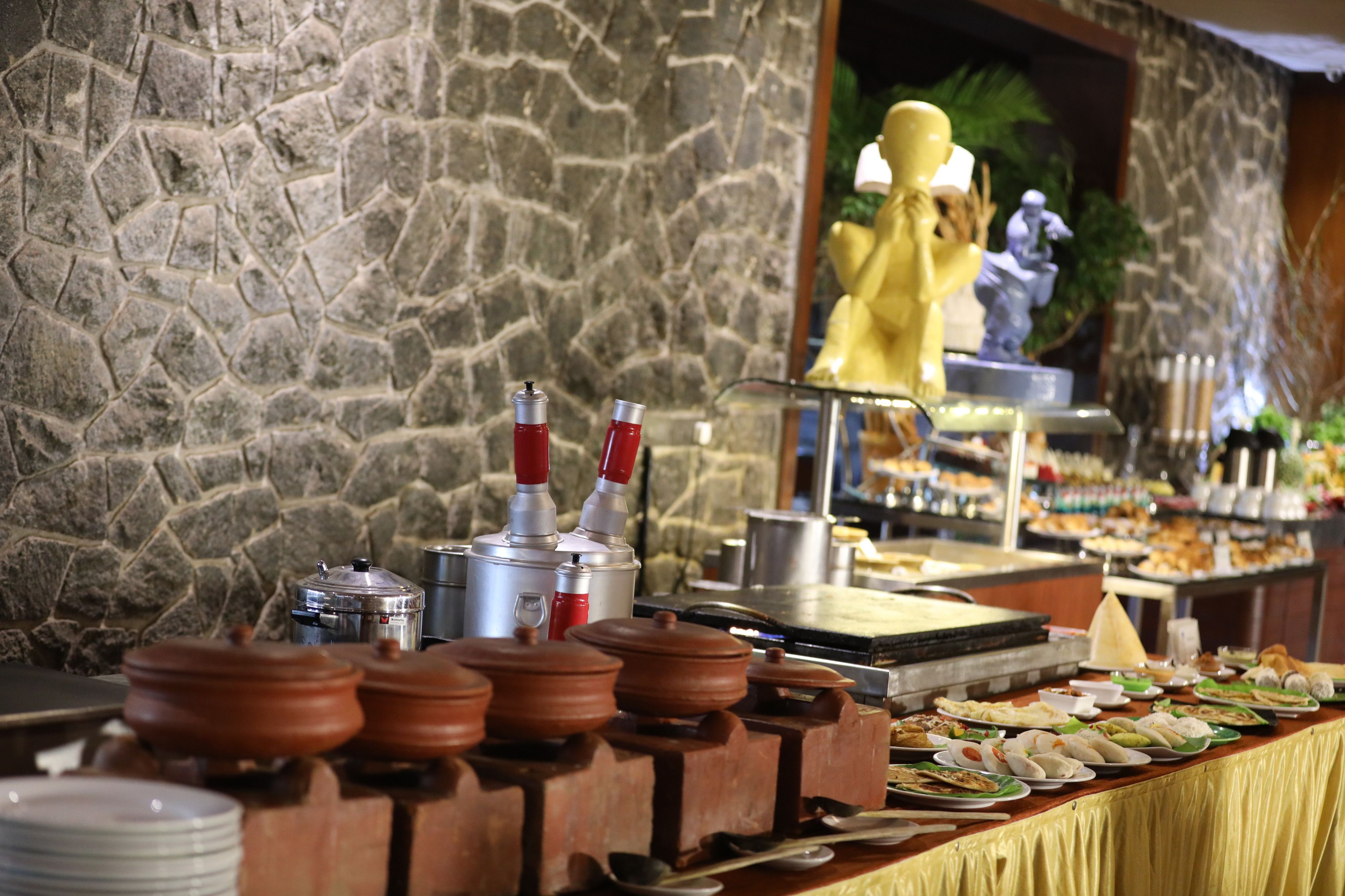 A buffet with various dishes and condiments, a stone wall, and a statue in the background.