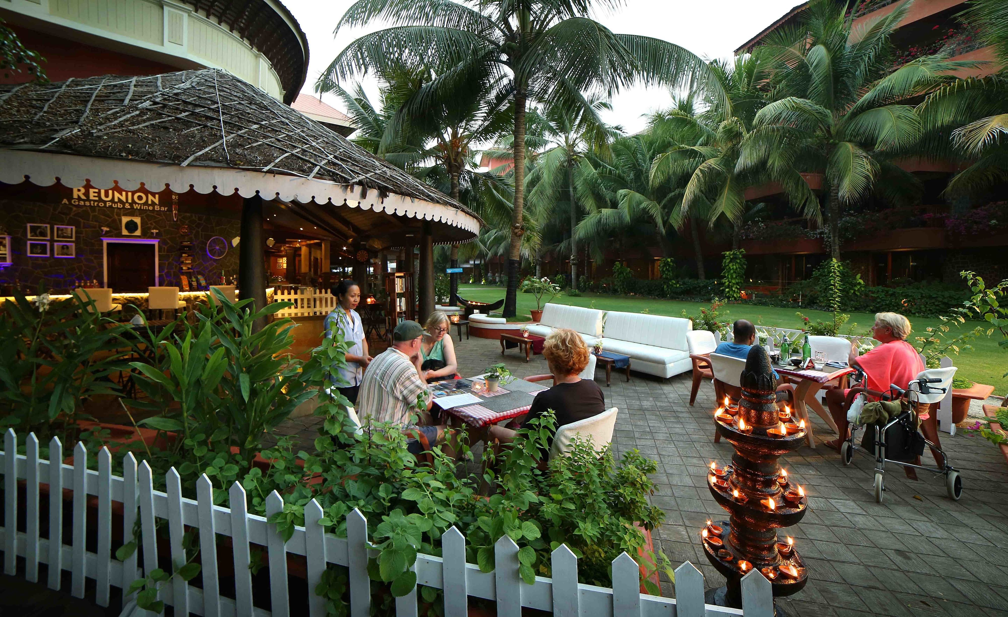 An outdoor seating area with tables and chairs, surrounded by lush greenery and palm trees.