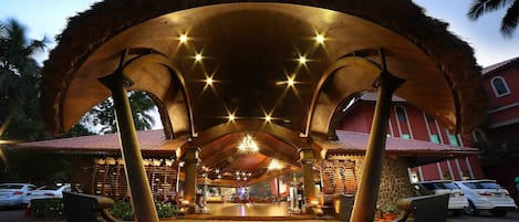 A covered outdoor area with a boat-shaped structure, columns, and a thatched roof.