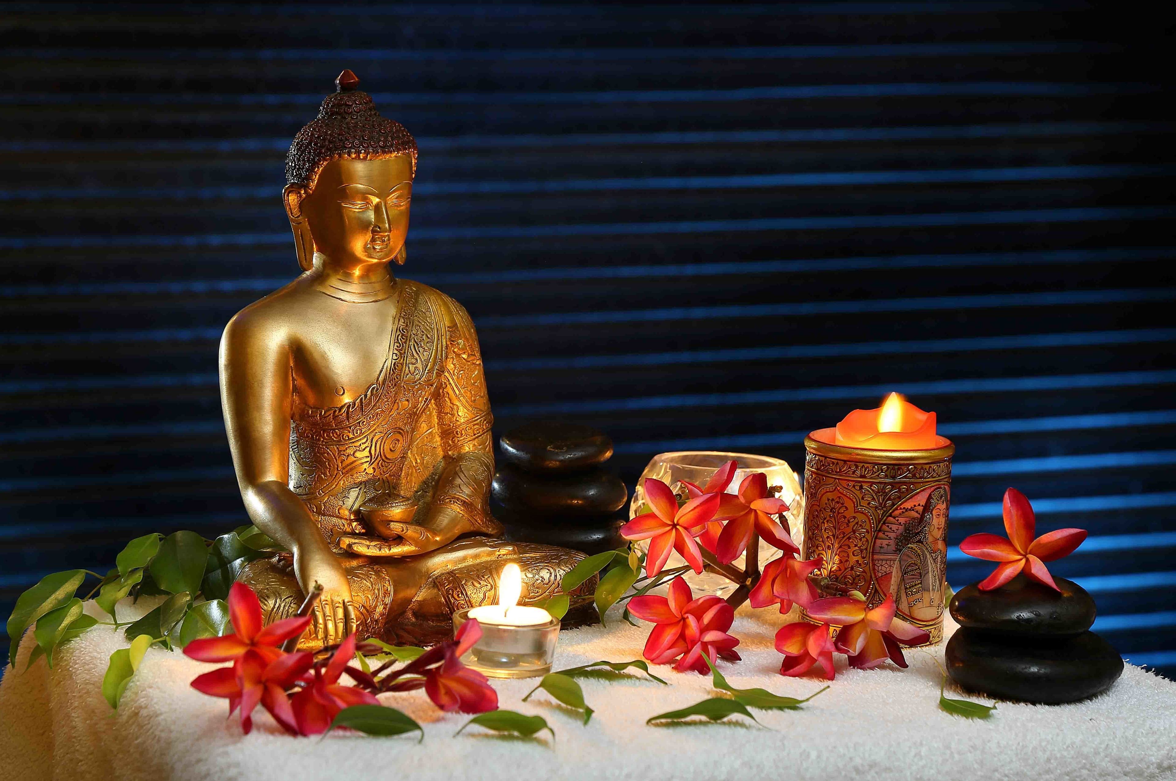 A golden Buddha statue, a candle, and tropical flowers on a white surface.