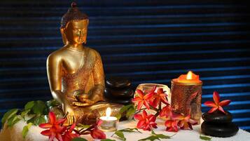 Una estatua dorada de Buda, una vela y flores tropicales sobre una superficie blanca.