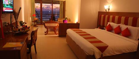 A hotel room with a bed, a desk, a chair, a television, and a view of the ocean through a sliding door.