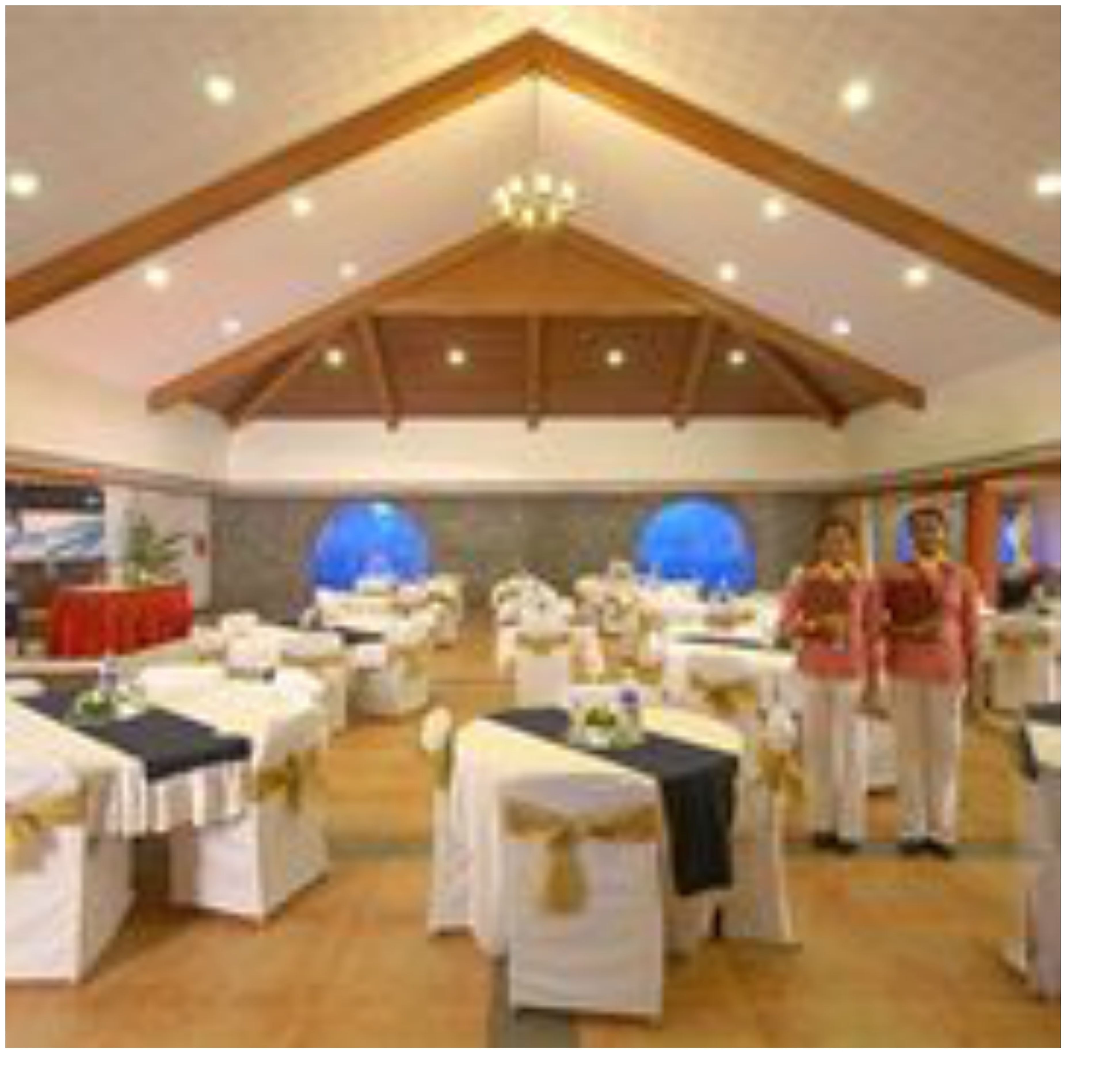 A banquet hall with tables set for events, wooden beams on the ceiling, and a chandelier.