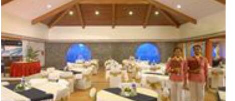Un salón de banquetes con mesas dispuestas para eventos, vigas de madera en el techo y una araña.