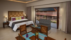Habitación de hotel con cama, sofá, mesa de comedor y balcón con vistas.