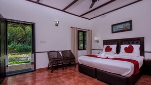 A hotel room with a bed, two chairs, a window, and a door leading to a garden. - Paradise Resorts (Kottayam)