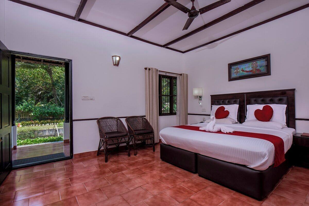 A hotel room with a bed, two chairs, a window, and a door leading to a garden.