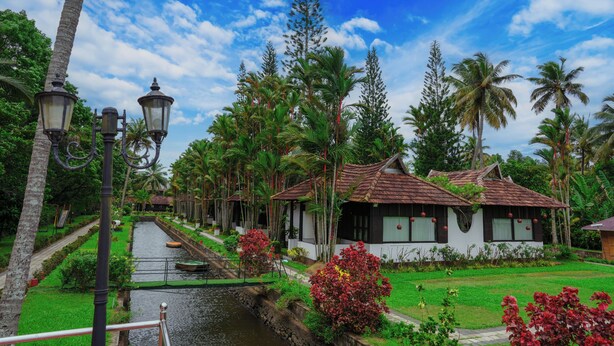 A traditional house with a tiled roof, surrounded by lush greenery and palm trees. - Paradise Resorts (Kottayam)