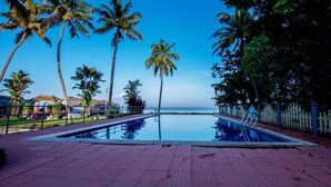 A swimming pool with a view of the ocean, surrounded by palm trees and a fence. - Paradise Resorts (Kottayam)
