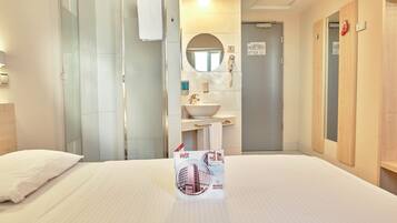 Habitación de hotel con cama, baño con lavamanos, espejo y ducha.