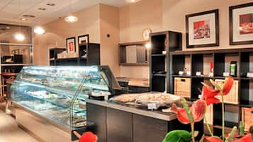 Mostrador de una panadería con un expositor de vidrio lleno de pasteles, una caja registradora y un reloj en la pared.