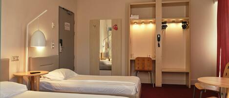 A hotel room with two beds, a desk, a chair, a mirror, and a red curtain.