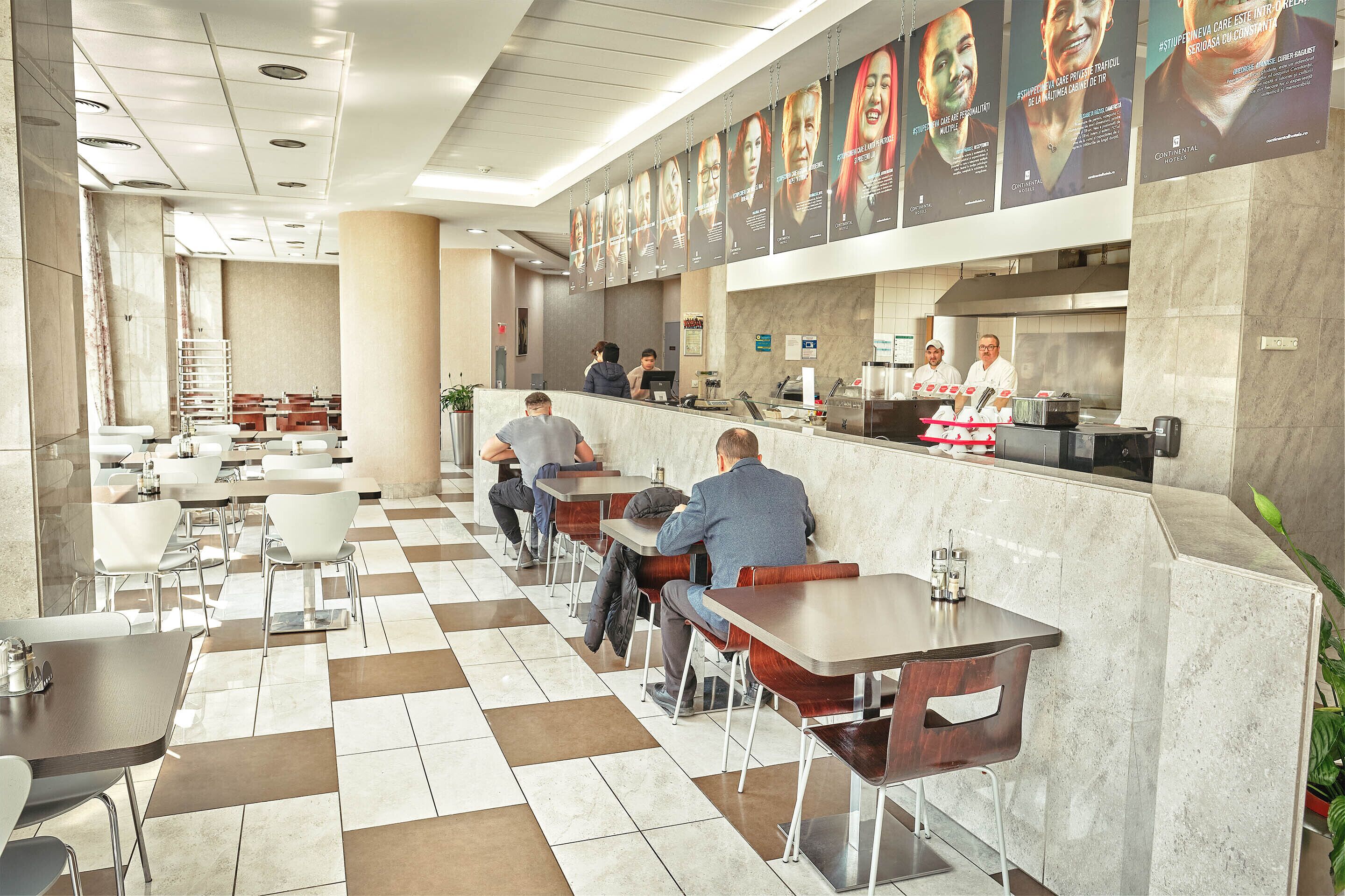 A modern restaurant with a checkered floor, marble walls, and a long counter with staff.