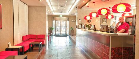 A hotel lobby with red seating, a reception desk, and a tiled floor.