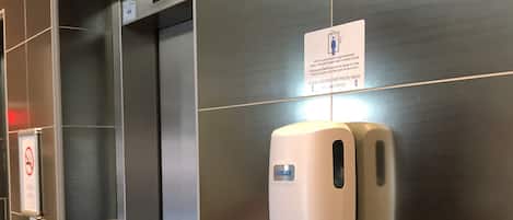 Un ascenseur doté d’un écran numérique, d’un distributeur de gel hydroalcoolique et d’un panneau indiquant les règles d’utilisation de l’ascenseur.