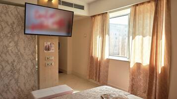 Une chambre d’hôtel équipée d’un lit, d’un téléviseur fixé au mur, d’une douche et d’une fenêtre avec des rideaux.