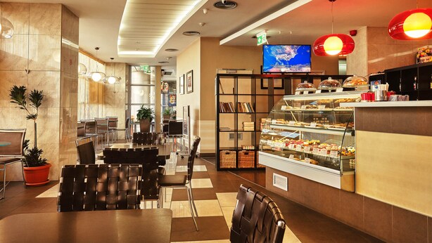 A modern hotel lobby with a dining area, a buffet, and a TV screen. - Hello Hotels Bucharest (Bucharest)