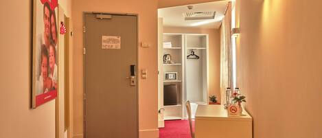 A hotel hallway with a red carpet, a white reception desk, a mirror, and a coat rack.