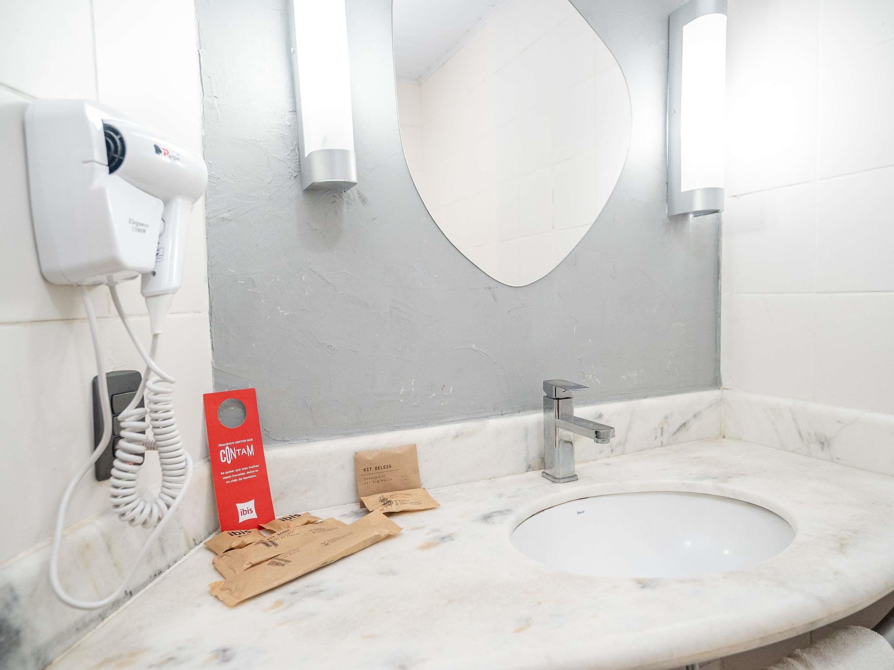 Un baño con lavamanos de mármol, espejo, secador de pelo y una caja roja con la etiqueta 'CONTAM'.
