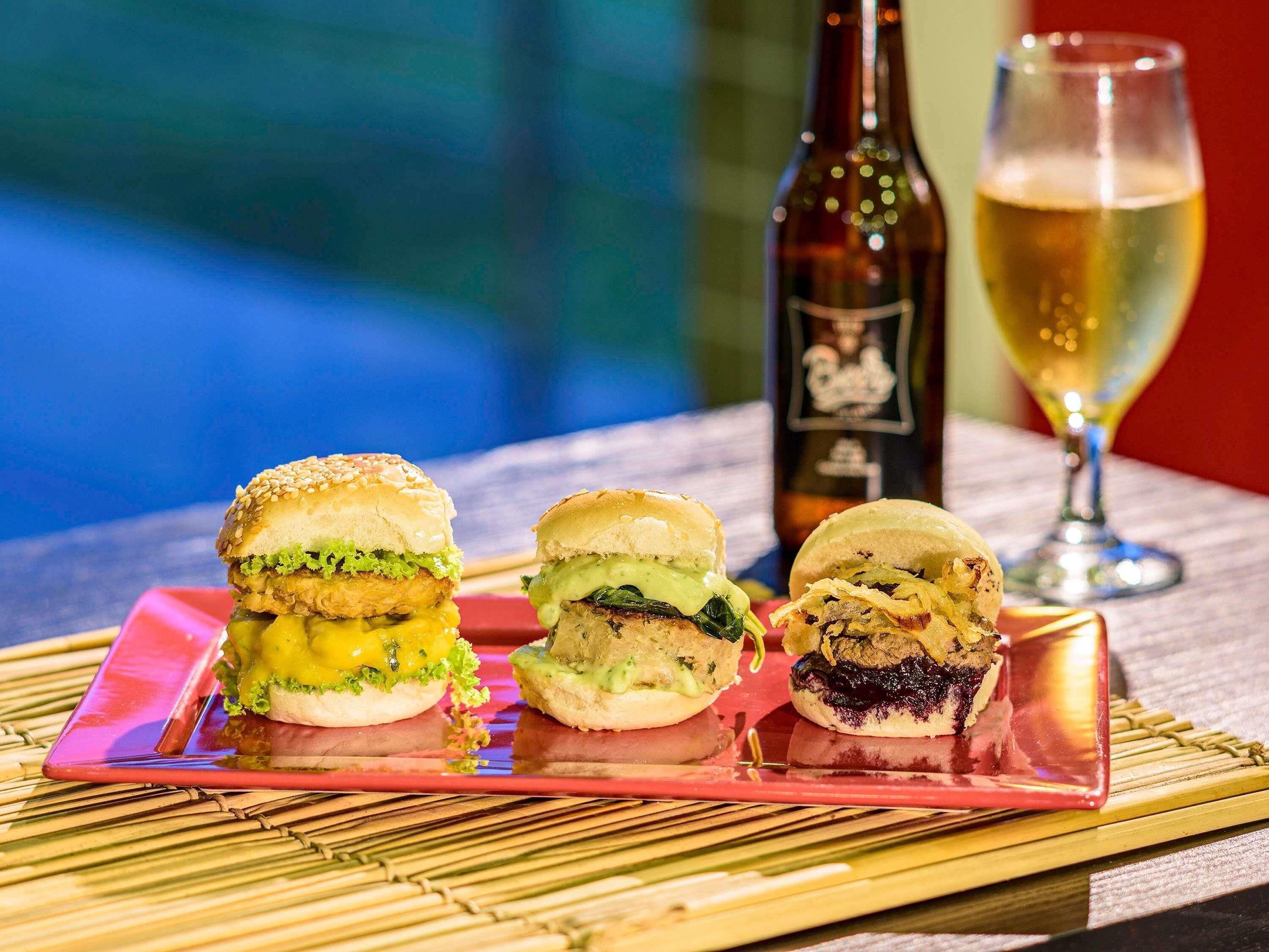 Three burgers on a tray, a bottle, and a glass of beer.