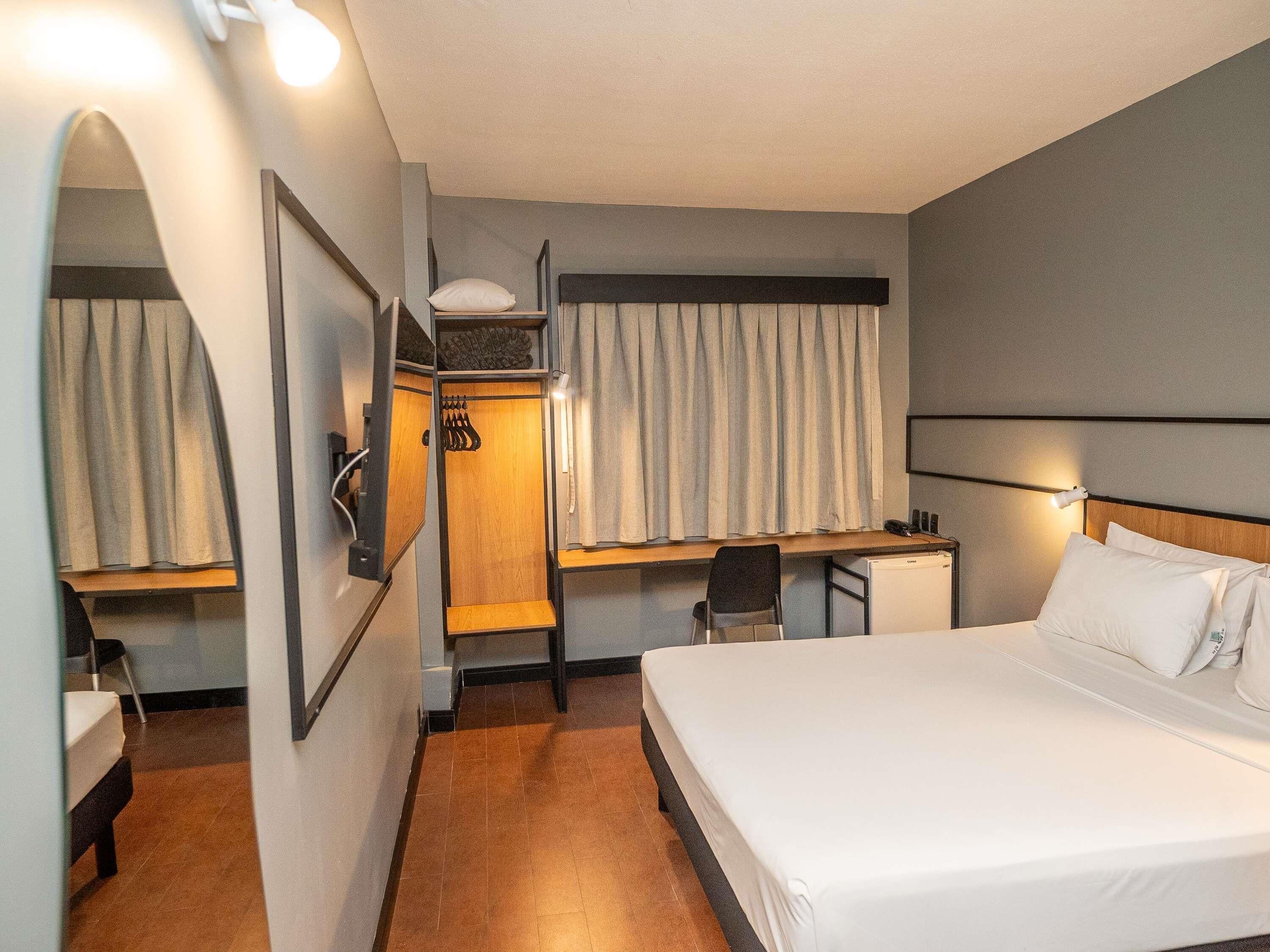 A hotel room with a bed, a desk, a chair, a wardrobe, and a mirror.