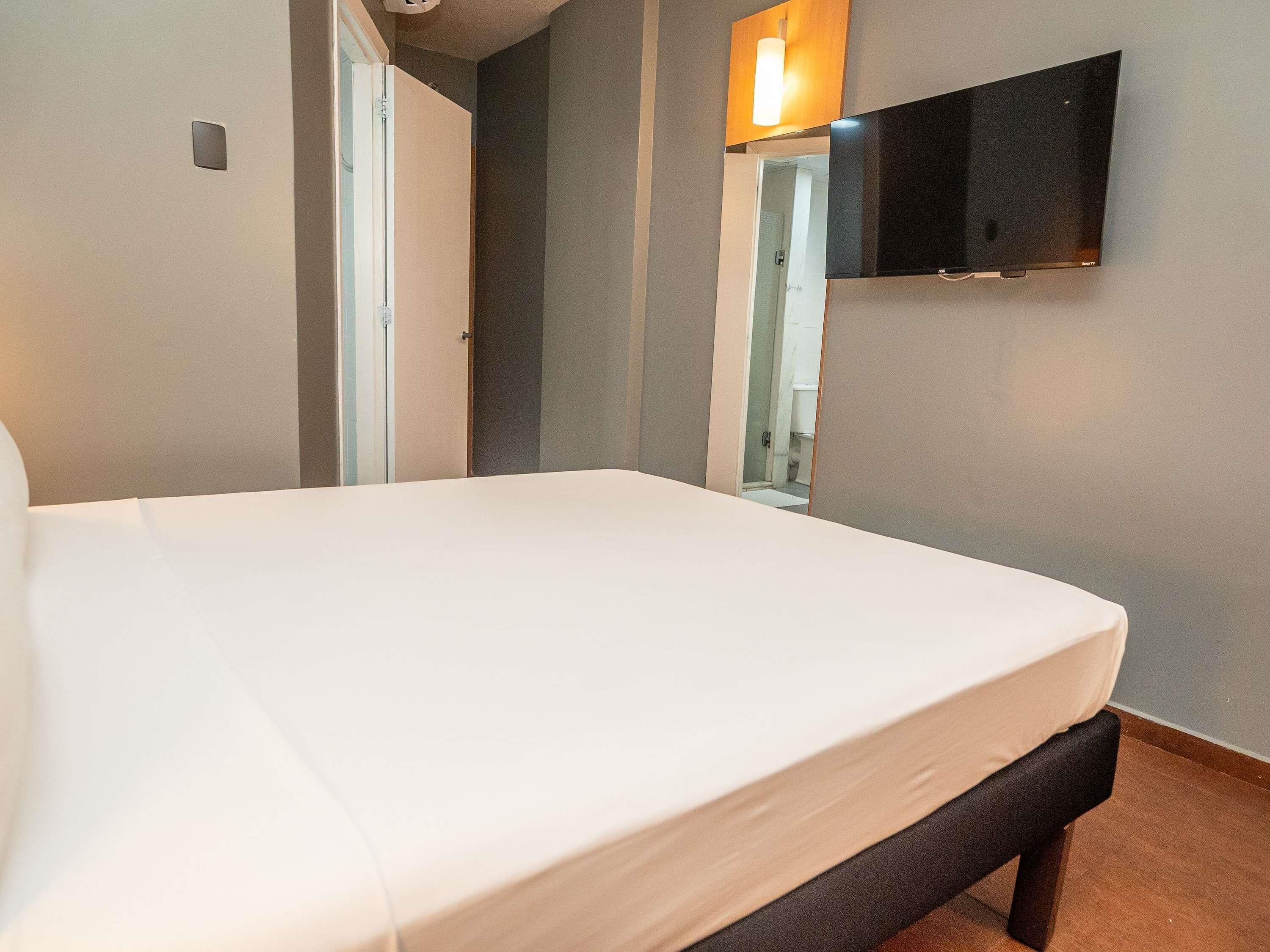A hotel room with a bed, a television mounted on the wall, and a door leading to a bathroom.