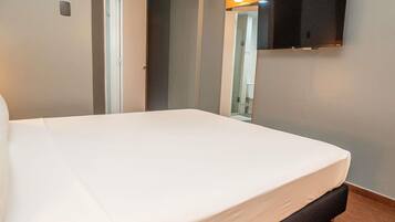 A hotel room with a bed, a television mounted on the wall, and a door leading to a bathroom.