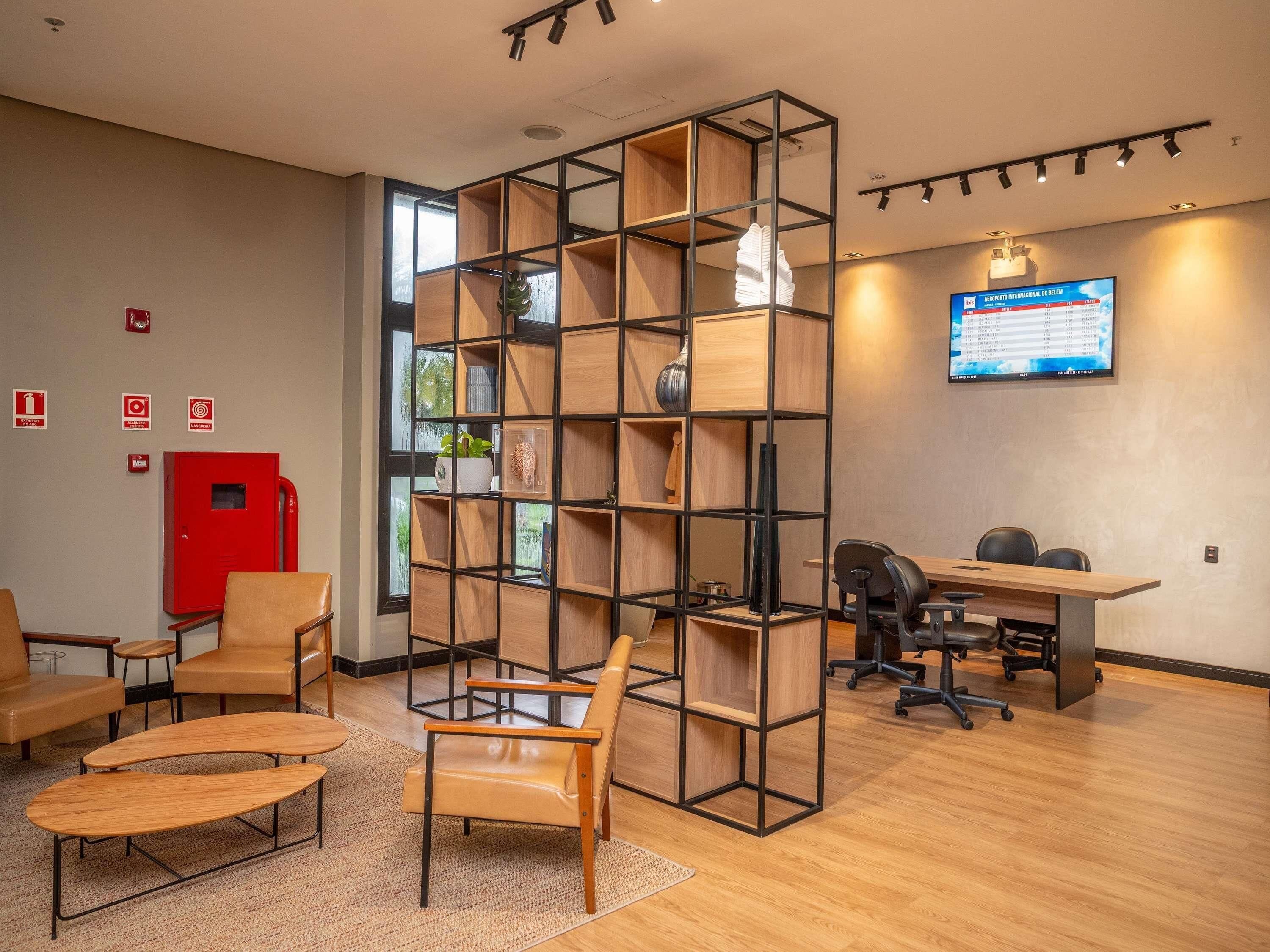 Um espaço de escritório moderno com uma unidade de estantes central, uma mesa com cadeiras de escritório e uma televisão fixada exibindo uma apresentação.