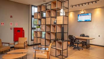 Um espaço de escritório moderno com uma unidade de estantes central, uma mesa com cadeiras de escritório e uma televisão fixada exibindo uma apresentação.