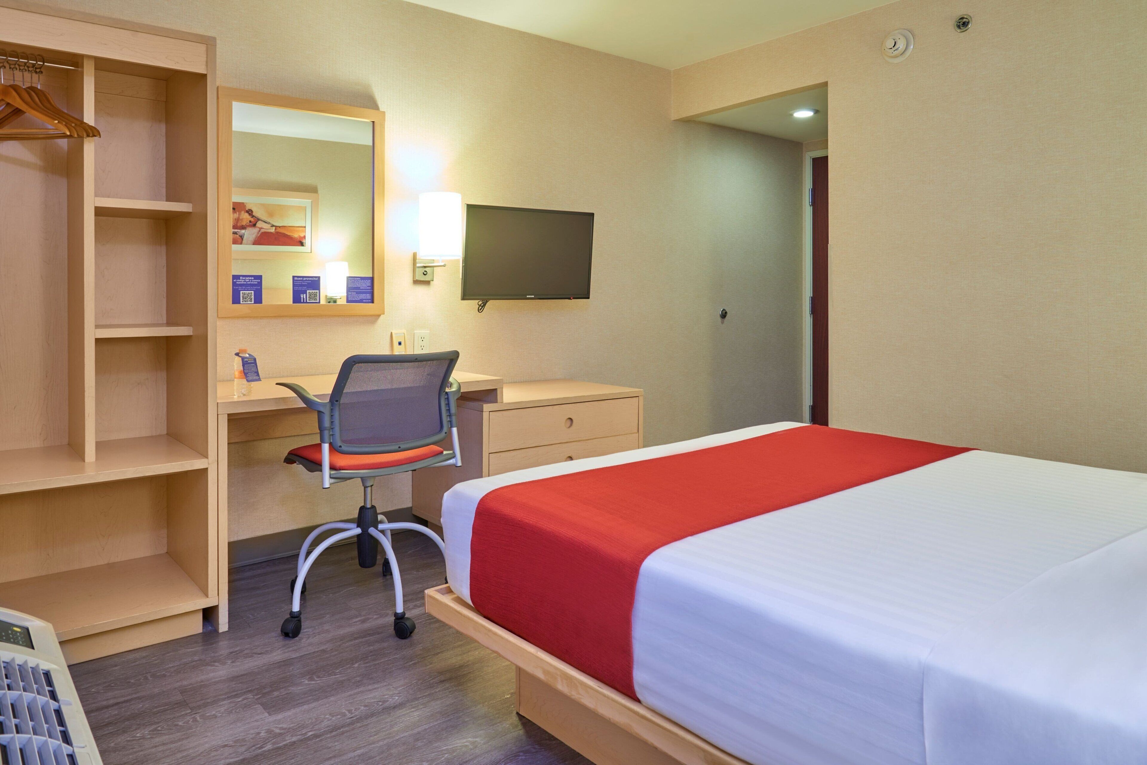 A hotel room with a bed, desk, chair, and a TV.
