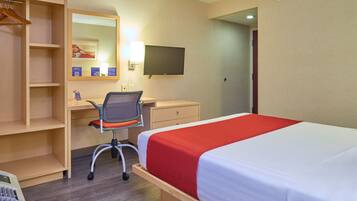 A hotel room with a bed, desk, chair, and a TV.