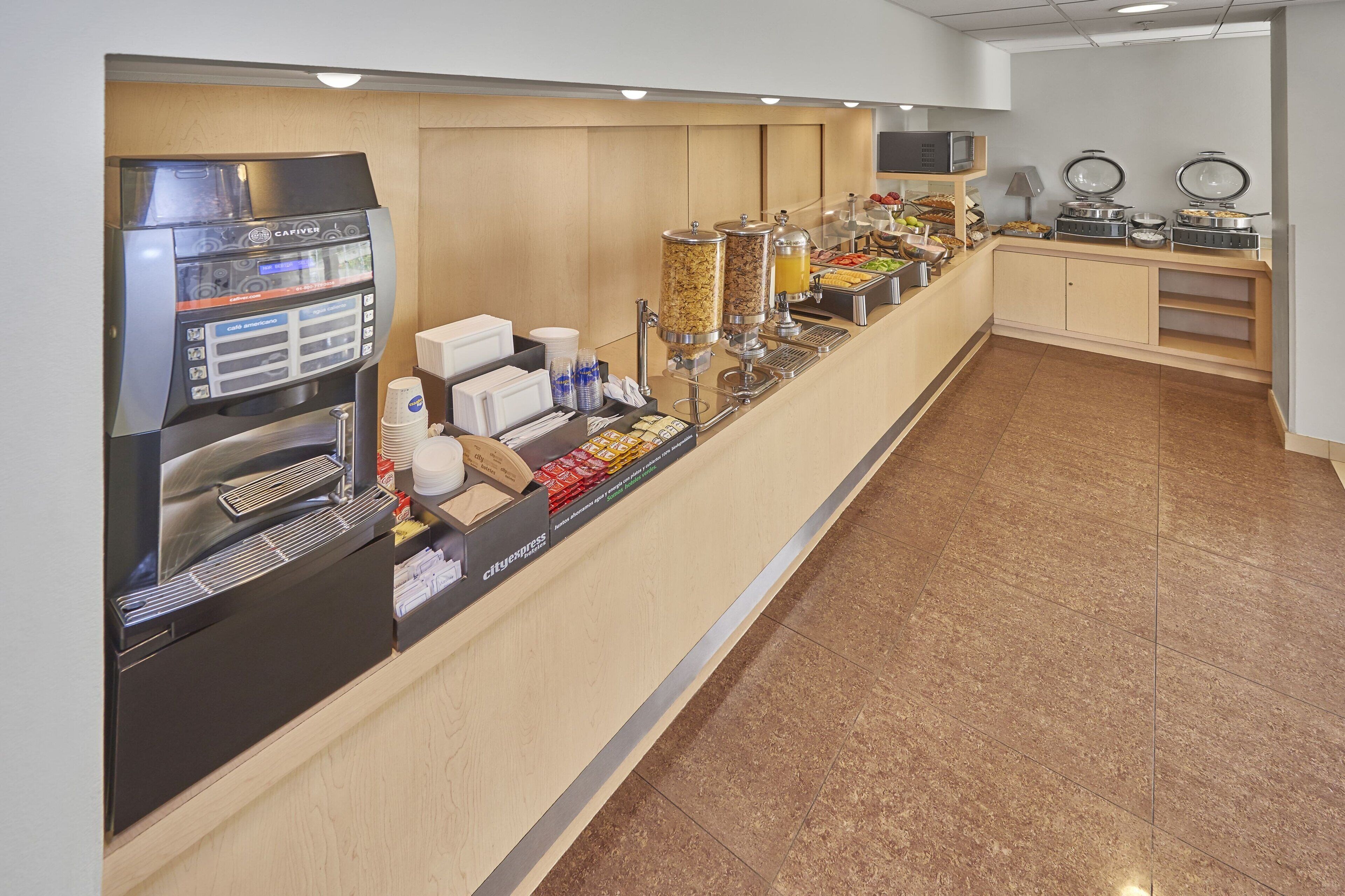 Una estación de desayuno autoservicio con una máquina de café, dispensadores de cereales y diversas opciones de alimentos.