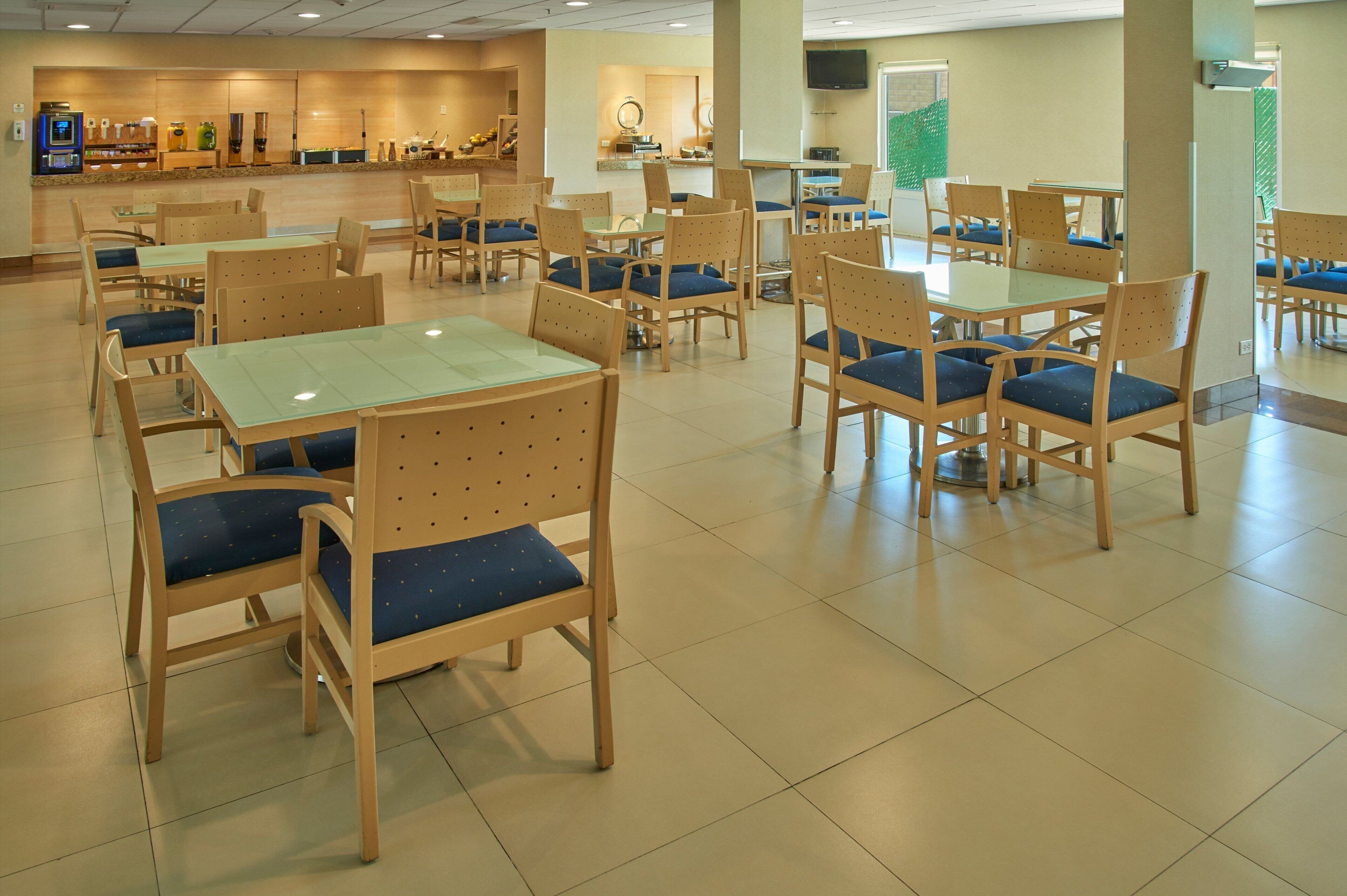 A spacious dining area with multiple tables and chairs, a counter with a display, and a television mounted on the wall.