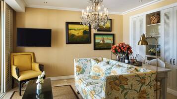 Una sala de estar con un sillón amarillo, un sofá con tapicería floral, un televisor de pantalla plana y una araña.
