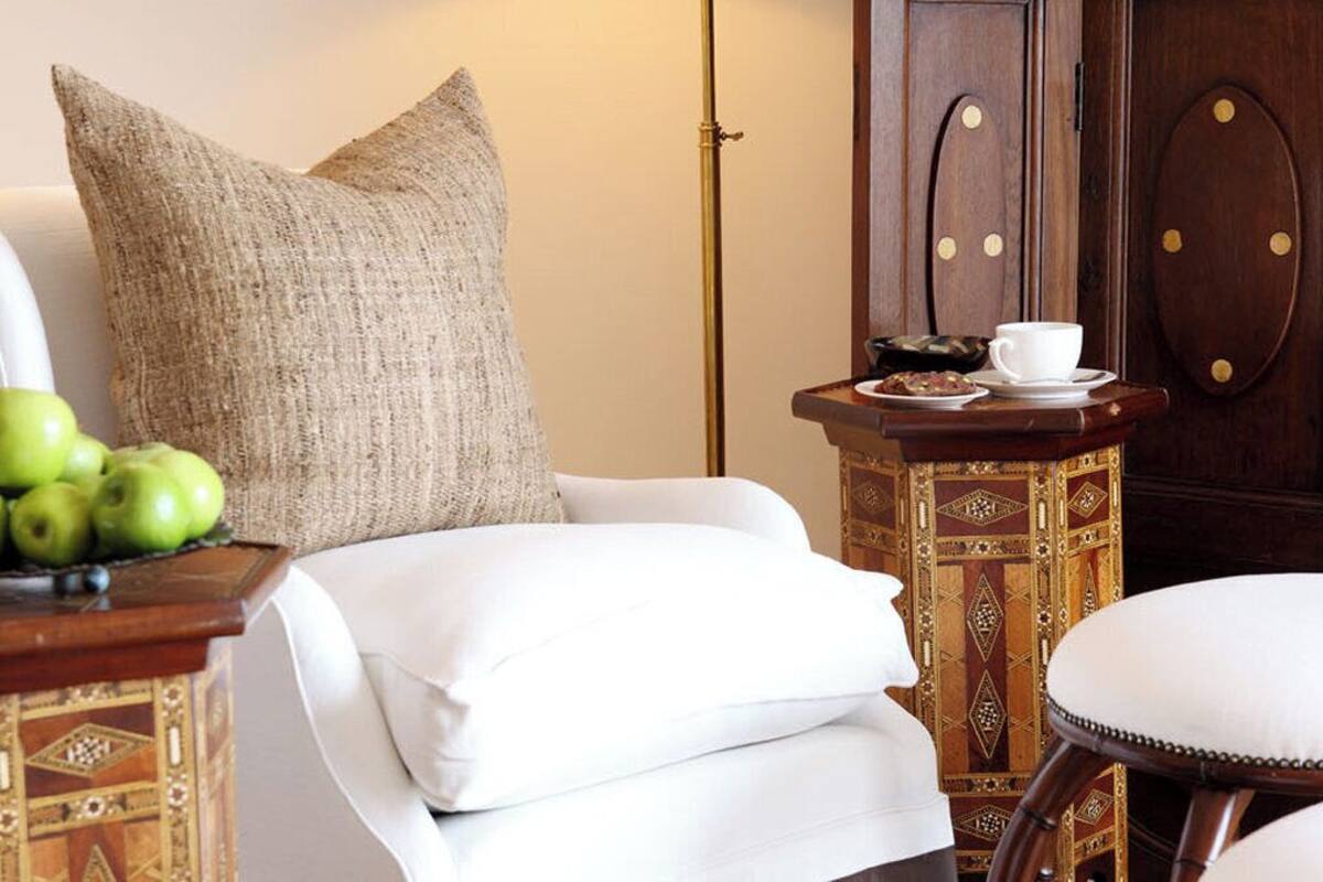 A cozy room with a white sofa, a patterned ottoman, a small table with a cup and pastries, and a decorative cabinet.