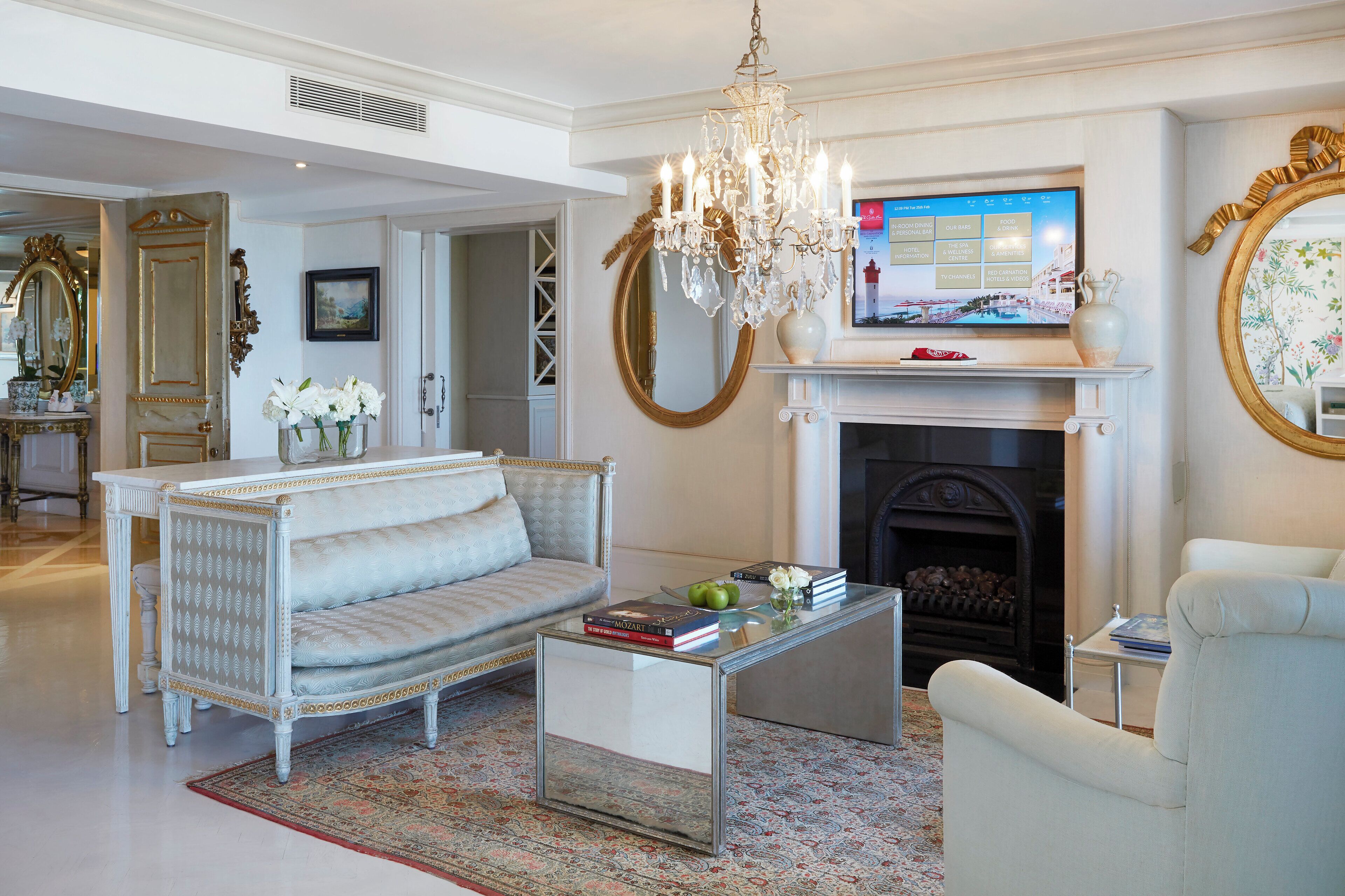 A living room with a sofa, armchair, coffee table, fireplace, television, and decorative mirror.
