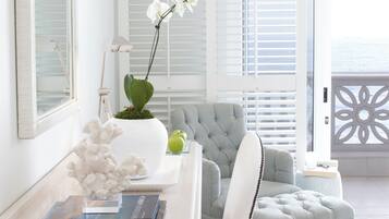 A modern living room with a white sofa, a side table with books and a potted plant, and a view of the ocean through large windows.