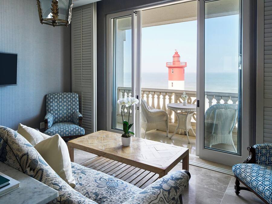 Un balcón con vistas a un faro rojo, un sofá, sillas estampadas y una mesa de madera con una planta en maceta.