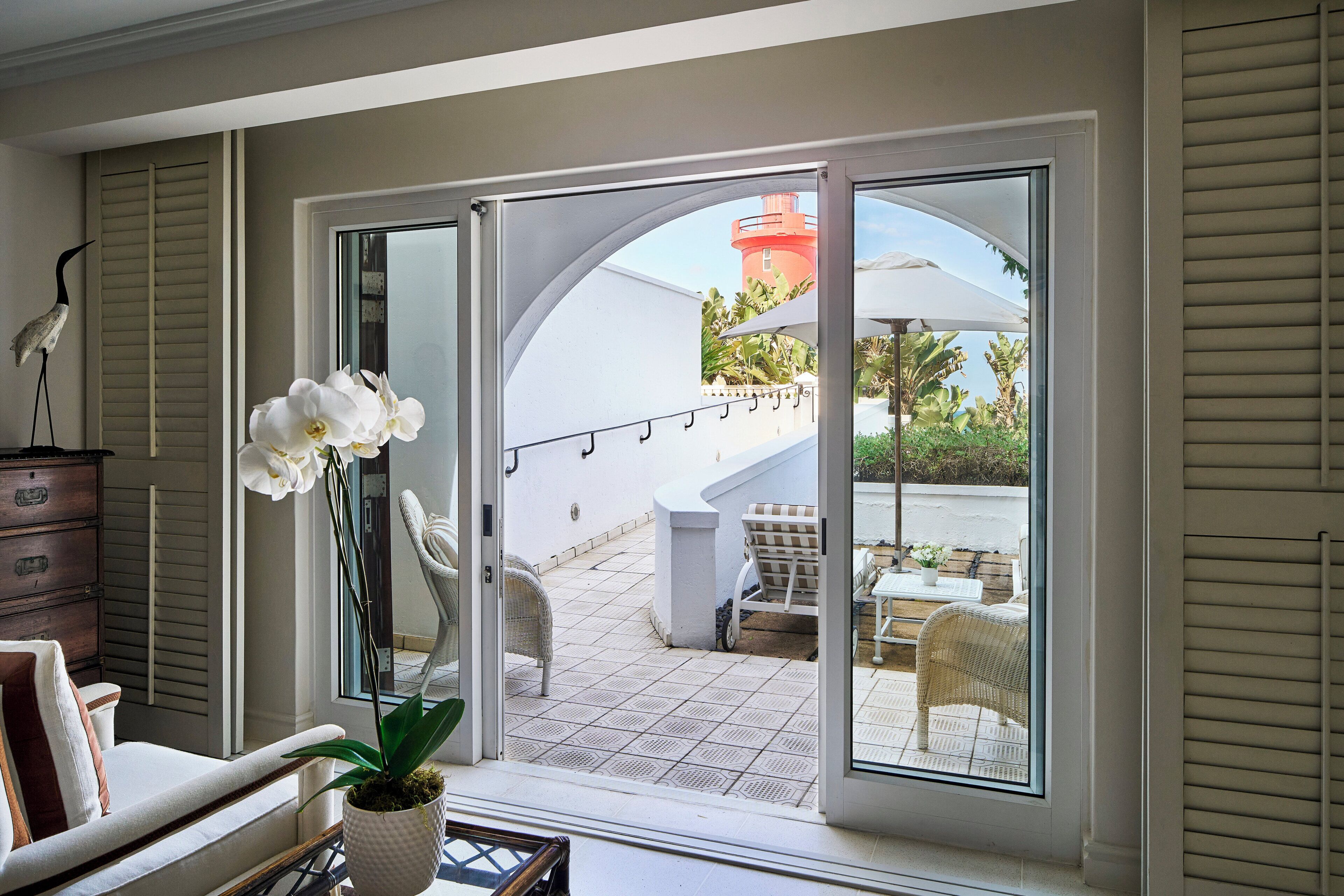 A room with a view of an outdoor patio, a wicker chair, a white sofa, and a potted orchid.