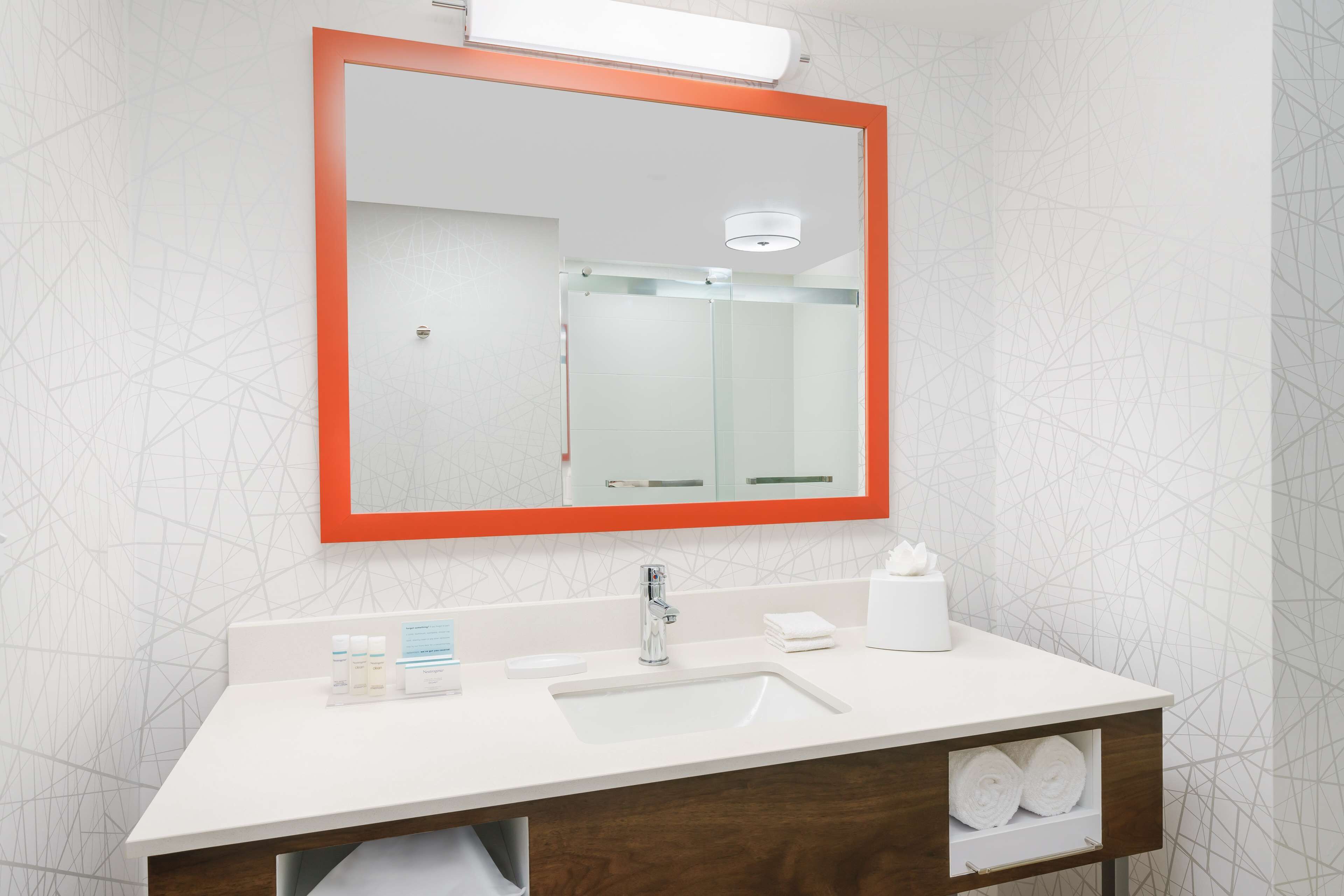 Un baño con un lavamanos blanco, un espejo con marco naranja y un perchero para toallas.