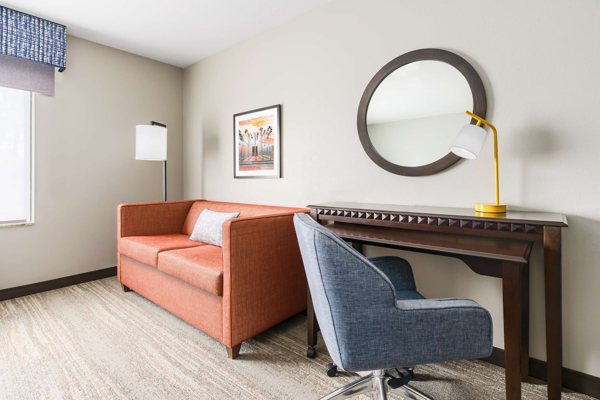 A room with a sofa, a desk, a chair, a lamp, and a framed picture on the wall.