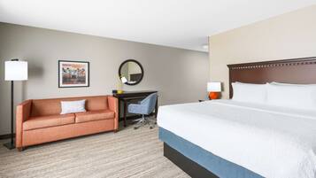 A hotel room with a large bed, a sofa, a desk, and a chair.