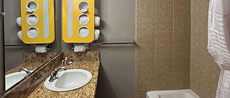 A bathroom with a granite countertop, a sink, a mirror, and a shower area.