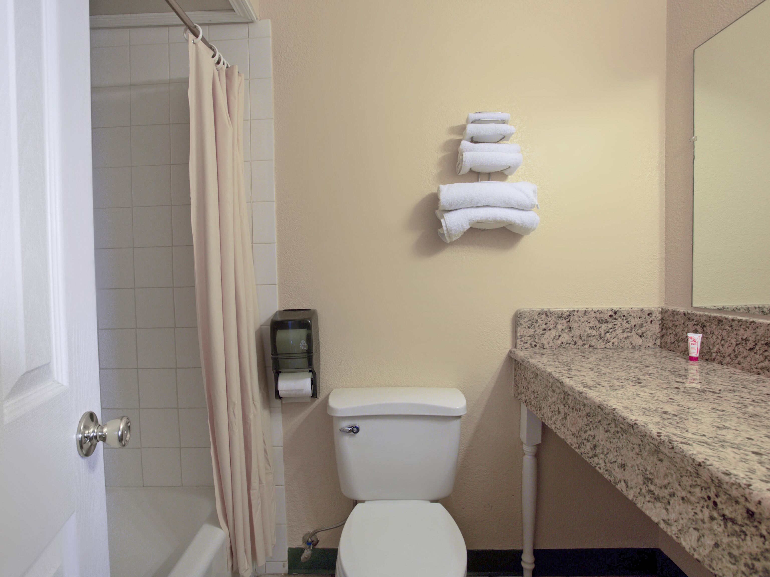 Une salle de bain comprenant des toilettes, un porte-serviettes avec des serviettes, un rideau de douche et un distributeur de savon.