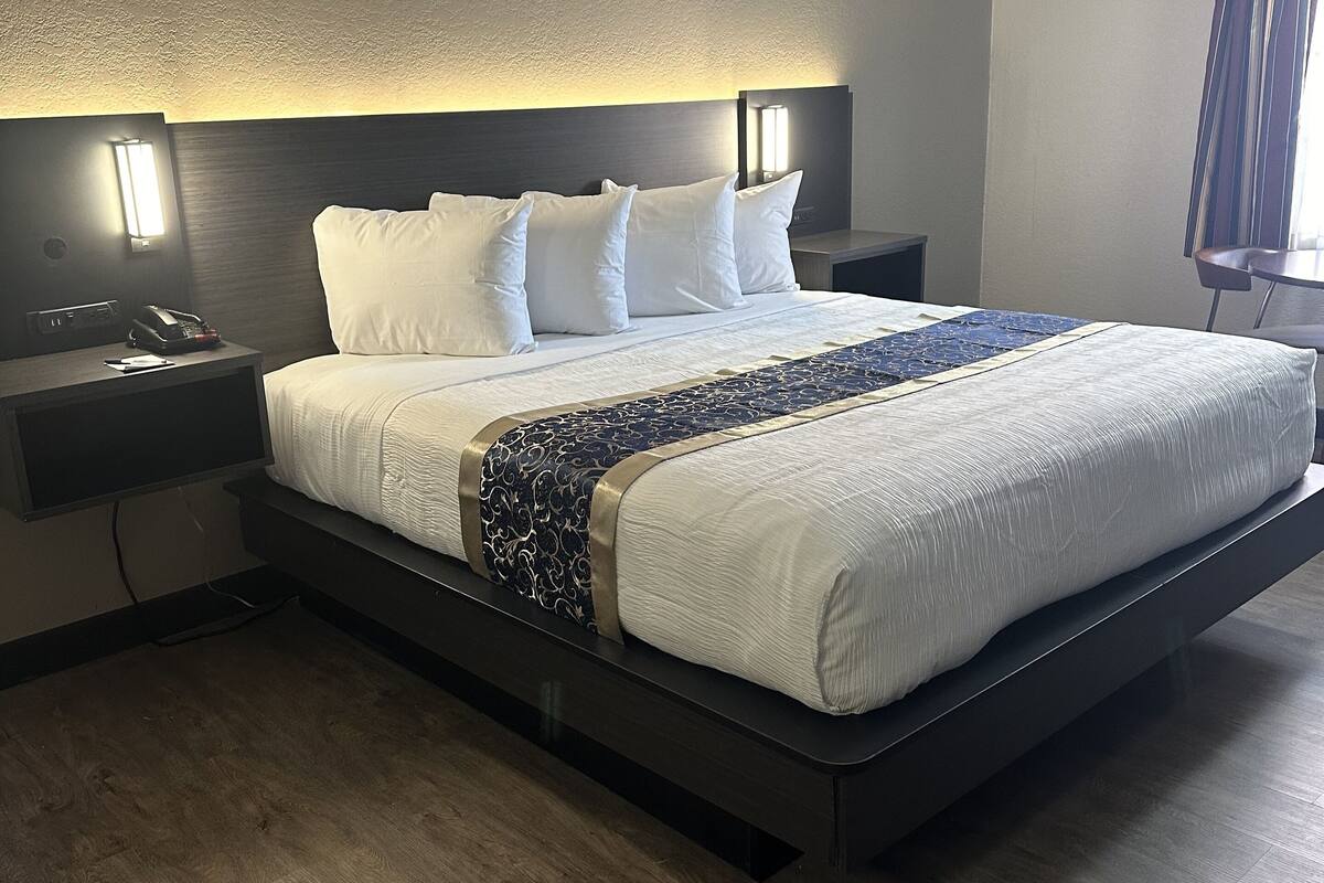 Una habitación de hotel moderna con una cama grande, lámparas de noche, una mesita y suelo de madera.